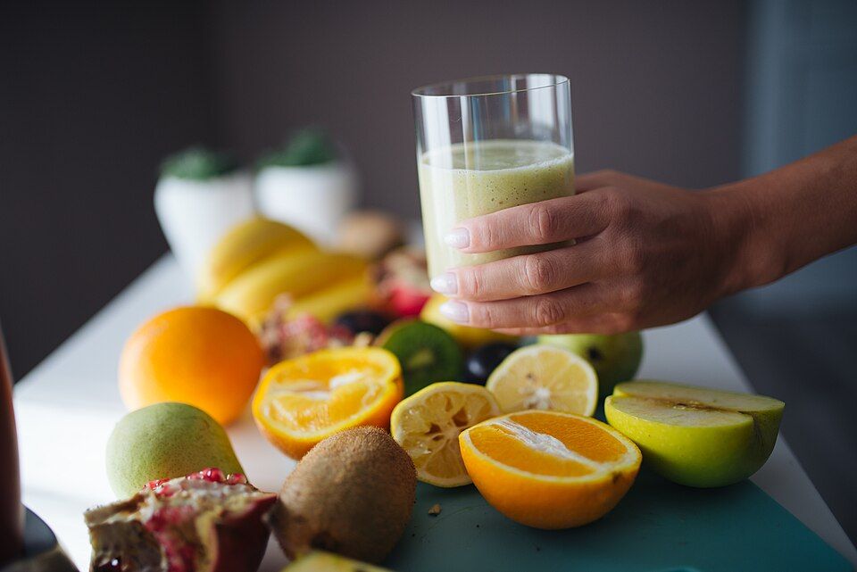 A green smoothie in a glass surrounded by fresh fruit