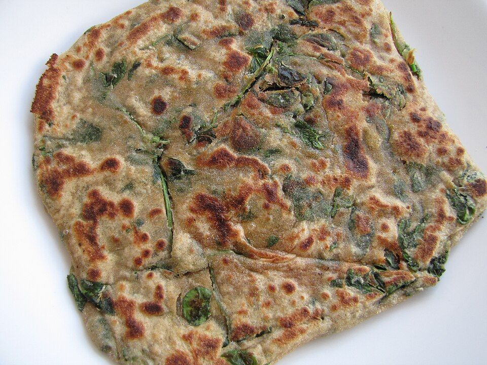 A golden methi paratha with visible fresh fenugreek leaves